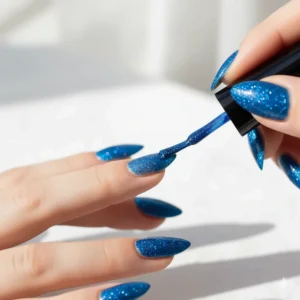 Step-by-step image showing the first coat of blue glitter nail polish being applied.