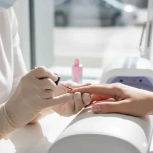 A nail technician carefully applying pink gel nail polish to a customer's nail with a brush.