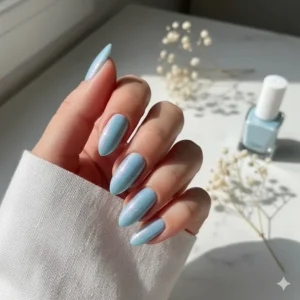 A model's hand with perfectly manicured nails painted with a shimmering light blue gel nail polish shade.