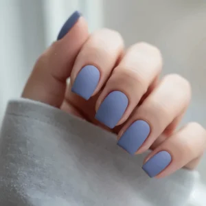 Close-up shot of fingernails wearing a matte periwinkle nail polish finish, highlighting the smooth, velvety texture.