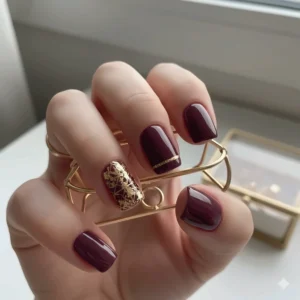 A stylish nail art design using plum nail polish as the main color with a gold accent nail.