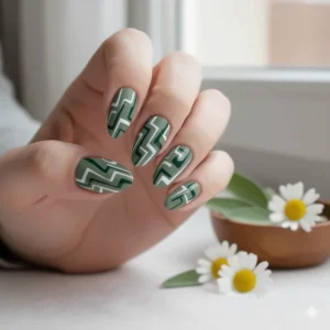 Funky, abstract sage green nail polish design with white and darker green geometric swirls and lines.