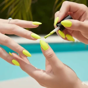 Close-up of a brush applying a second coat of opaque neon yellow nail polish to ensure full coverage.