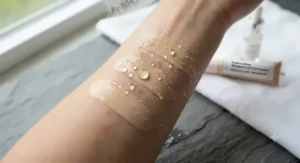 Water droplets beading on the surface of a waterproof full coverage concealer for acne scars swatch.