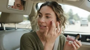 A woman applying a contour stick for on-the-go touch-ups while sitting in a car