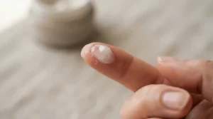 Demonstrating finger application of a cream highlighter for a natural dewy look on bare skin